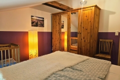 Lila Zimmer mit Doppelbett aus massiven Balken (180x200) und Kinderbettchen (60x120)